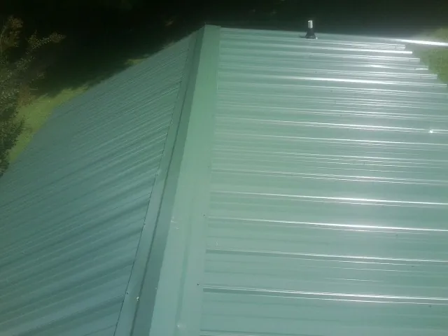 New green metal panels meeting at the ridge of a roof — Flat Roof Repair work by our crew in Howard